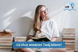 Kobieta o blond włosach, rozpuszczonych, w okularach, zapatrzona na bok, siedzi na podłodze i czyta książkę, obok niej kilka stosów książek.