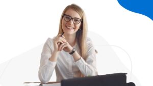 Uśmiechnięta kobieta w okularach, o długich blond włosach, w białej koszuli.