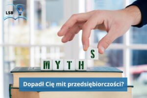 Ręka mężczyzny układa z klocków słowo MYTHS i kładzie je na książkach w twardej oprawie ułożonych jedna na drugiej.