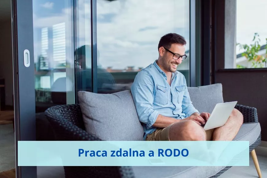 Mężczyzna siedzi na tapczanie i z uśmiechem pracuje na laptopie.