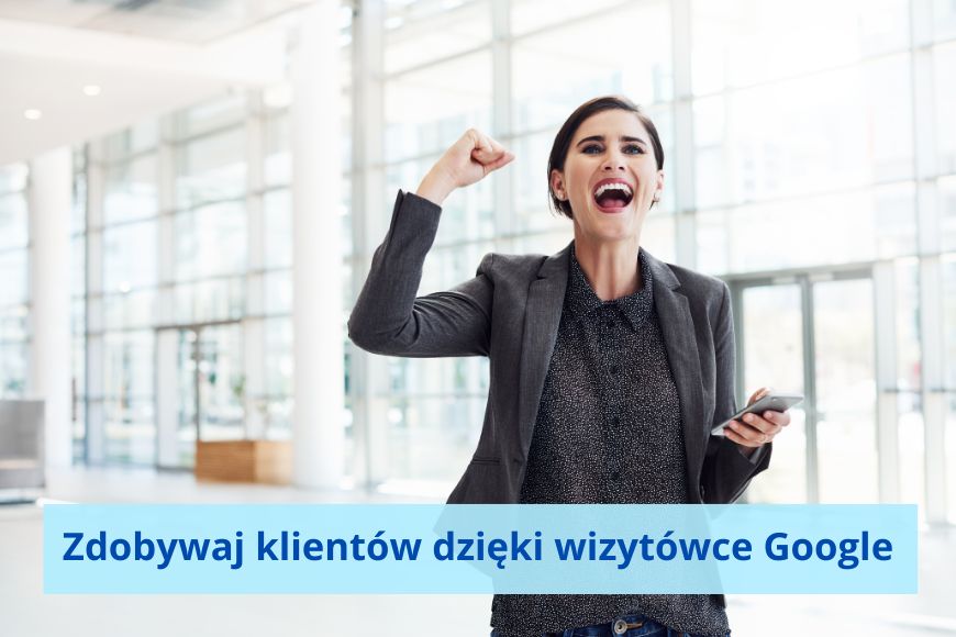 Kobieta w związanych ciemnych włosach, w grafitowej marynarce w jednej dłoni trzyma komórkę, drugą ma uniesioną w geście zwycięstwa. Szeroki uśmiech na twarzy