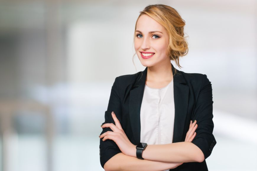 Uśmiechnięta kobieta o związanych blond włosach w czarnej marynarce i białej bluzce.
